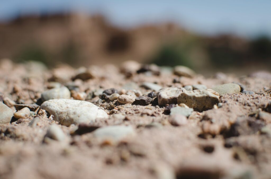 Detailed textured view of earthy natural terrain, featuring rocks and sand under daylight.